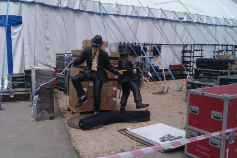 1991 Ford LTD Crown Victoria - Two statues dressed as musicians are positioned near event equipment and caution tape.
