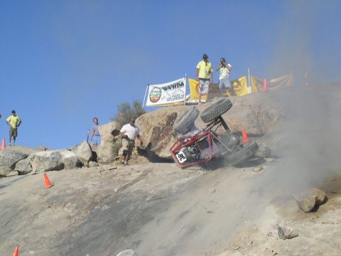 1979 Ford Bronco - An off-road buggy has flipped over during a competition on a rocky hill, with onlookers observing the scene.