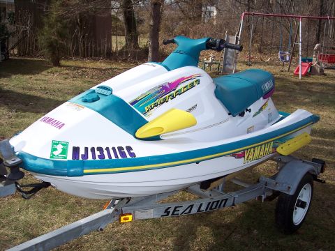 1996 Yamaha RA760 WaveRaider 2-P - A Yamaha WaveRunner jet ski sits on a trailer in a grassy yard with a swing set in the background.
