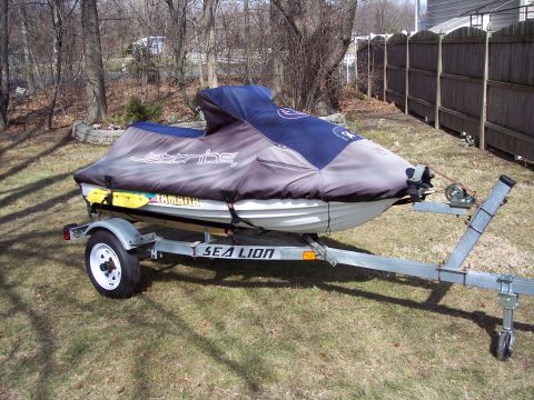 1996 Yamaha RA760 WaveRaider 2-P - Jet ski on a trailer, covered and parked on grass with a wooden fence in the background.