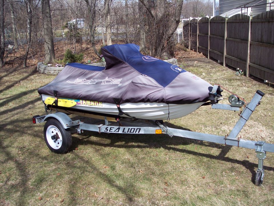 Jet ski covered with a blue and gray cover, on a Sea Lion trailer. Yamaha branding visible on the cover