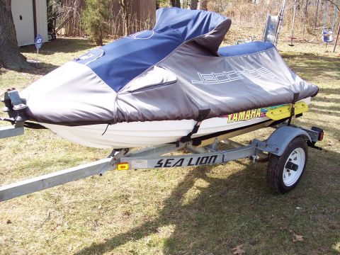 1996 Yamaha RA760 WaveRaider 2-P - A Yamaha jet ski is parked on a trailer in a grassy area, partially covered by a tarp.