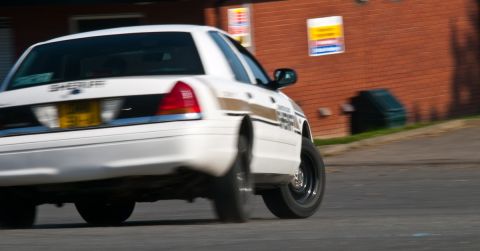 2001 Ford Crown Victoria - A white 2001 Ford Crown Victoria sheriff's car is captured from the rear as it drives on a road.