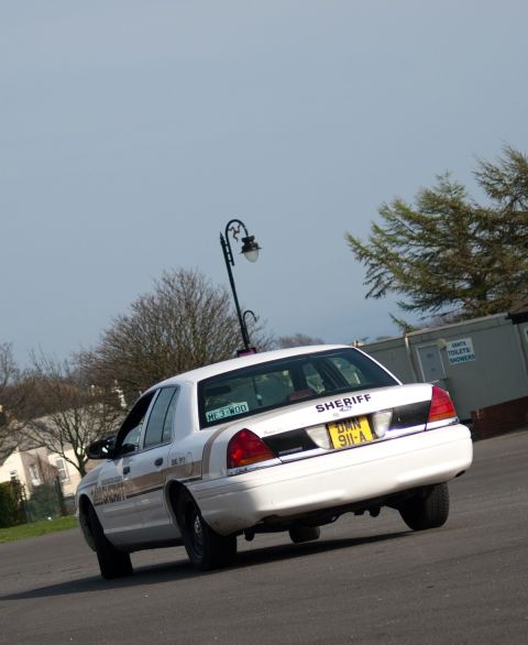 2001 Ford Crown Victoria - A white 2001 Ford Crown Victoria police car is seen from the rear, with 'SHERIFF' text on the trunk.