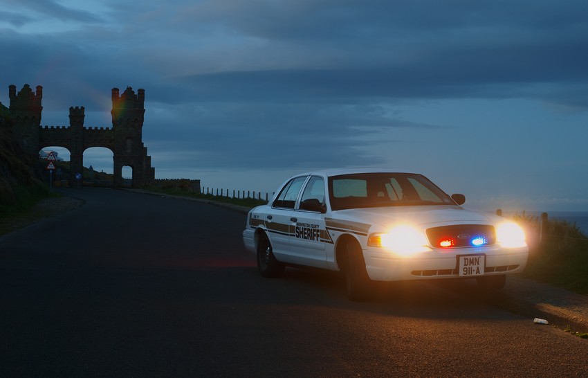 2001 Ford Crown Victoria police car with lights on, parked by a castle at dusk