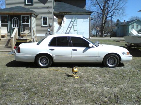1999 Mercury Grand Marquis - White sedan with tinted windows parked in a yard, with a house undergoing renovations behind it.