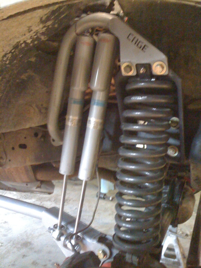 Close-up of custom suspension components including dual shocks and a coilover spring. The word 'CAGE' is visible on a bracket