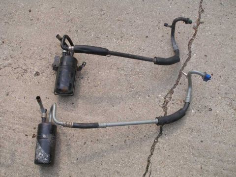 1997 Ford Taurus - Two AC accumulators and associated hoses are laid out on a cracked concrete surface.