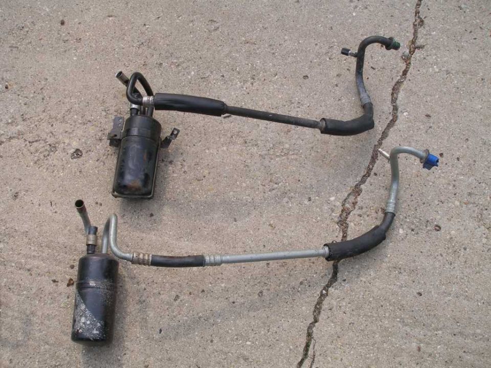 Two black AC accumulators with metal and rubber hoses on a cracked concrete surface