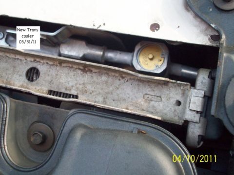 1998 Ford Crown Victoria - Close-up down into the front of an engine bay past the radiator support crossmember, showing hose fittings and a yellow-capped reservoir be…