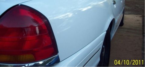 1998 Ford Crown Victoria - Tight low-angle detail of the driver-side rear corner of a white sedan, showing the red tail lamp lens with amber turn-signal section and c…