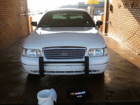 1998 Ford Crown Victoria - Head-on front view of a freshly washed white Ford Crown Victoria in a brick self-serve car wash bay, showing the horizontal-bar chrome gril…