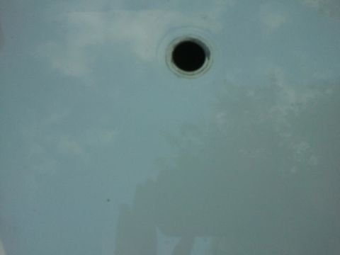 1998 Ford Crown Victoria - Close-up of a drilled round hole through a glossy white painted sheet metal panel, with bare metal visible at the cut edge and sky and tree…