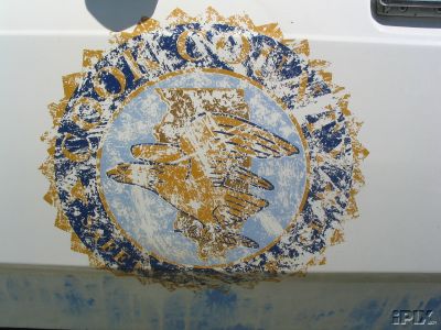 1991 Ford LTD Crown Victoria - Close-up of an emblem on the side of a white vehicle, showing an eagle and globe design.