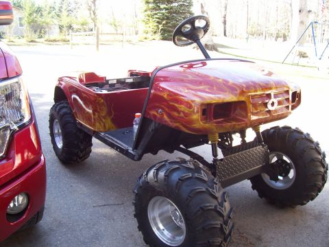 1978 Ford F-150 - A modified golf cart with flame paint and large off-road tires sits beside a red pickup truck.