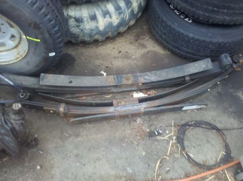 2003 Ford F-250 - Several leaf springs and tires are piled up on a dirty surface, likely in a garage or yard.