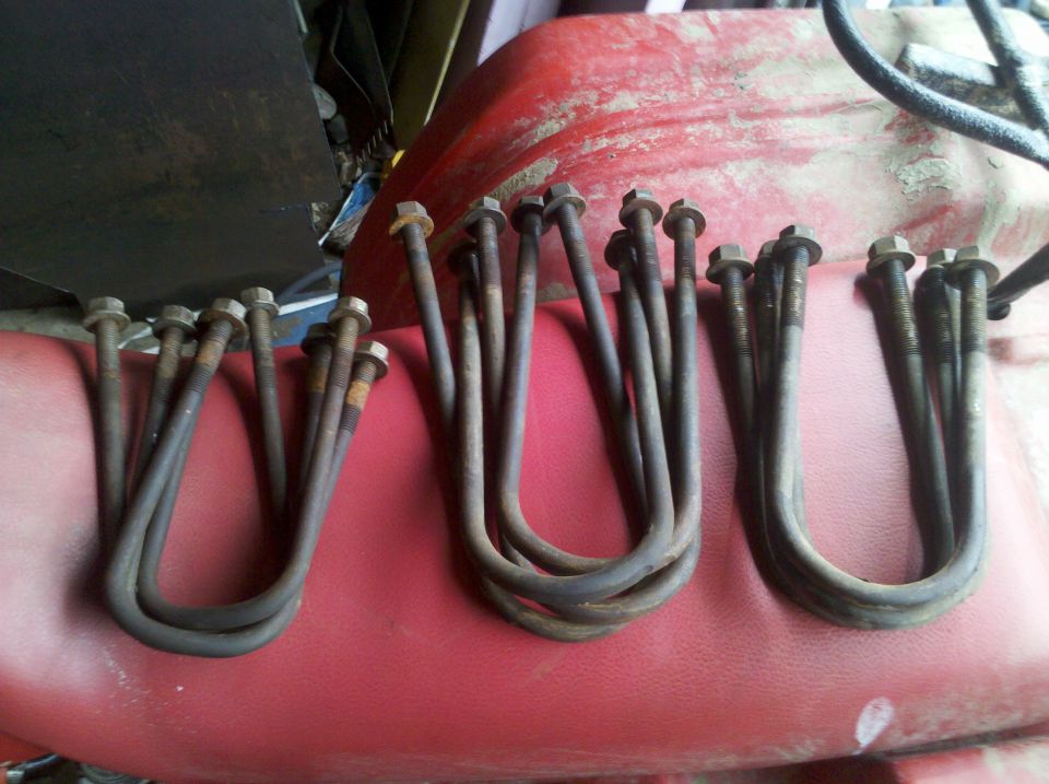 Several rusty U-bolts with nuts laid out on a red surface