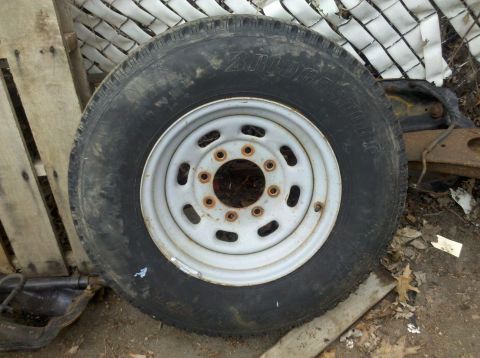 2003 Ford F-250 - A single truck wheel and tire is shown, resting on the ground near some wooden pallets and a fence.