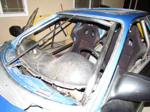1995 Ford Probe - Interior view of a modified blue car racing seats and a roll cage, with a damaged windshield.