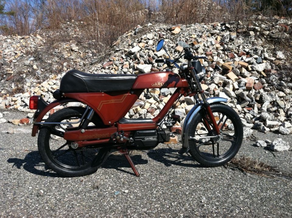 Red moped with black seat and wheels, side view. Text on frame reads 'Garelli'