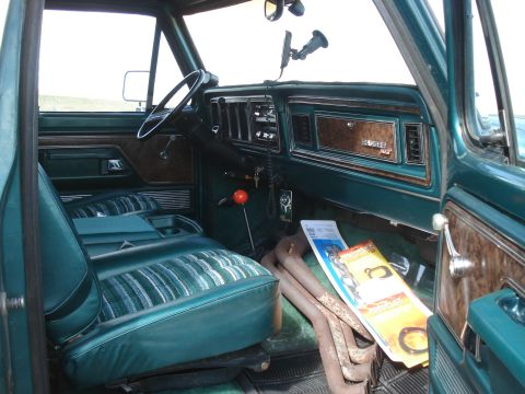 1979 Ford Bronco - The interior of a 1979 Ford Bronco features green striped seats, wood grain accents on the dashboard, and a prominent orange shifter.