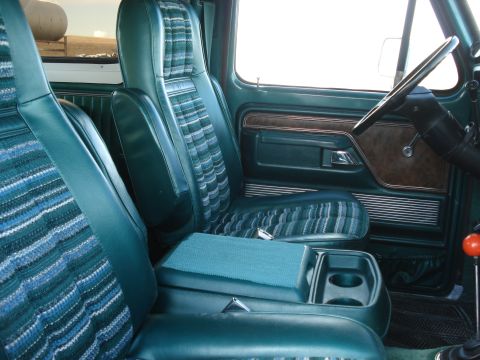 1979 Ford Bronco - The interior features teal vinyl seats with a patterned fabric insert and a brown wood-grain trim on the door panel.