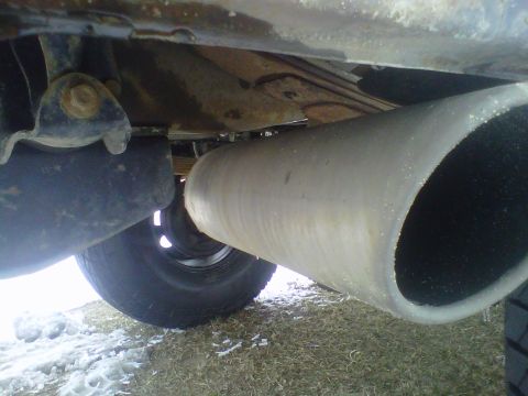 1994 Ford F-150 - The underside of a truck reveals a large exhaust pipe and a rear tire, with patches of snow on the ground.