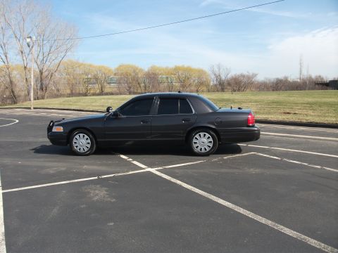 2001 Ford Crown Victoria - A dark gray 2001 Ford Crown Victoria sedan is parked in a lot under a clear sky.