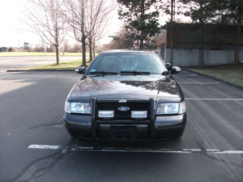 2001 Ford Crown Victoria - A black Ford Crown Victoria police car is parked in a lot, facing the camera with a push bumper and lights visible.