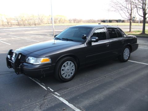 2001 Ford Crown Victoria - A dark gray 2001 Ford Crown Victoria police car is viewed from a three-quarter front angle in a parking lot.