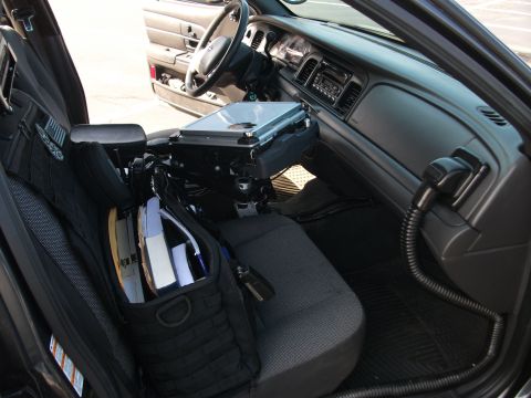 2001 Ford Crown Victoria - The interior of a 2001 Ford Crown Victoria police car, equipped with a laptop mount and a seat-back organizer filled with documents.