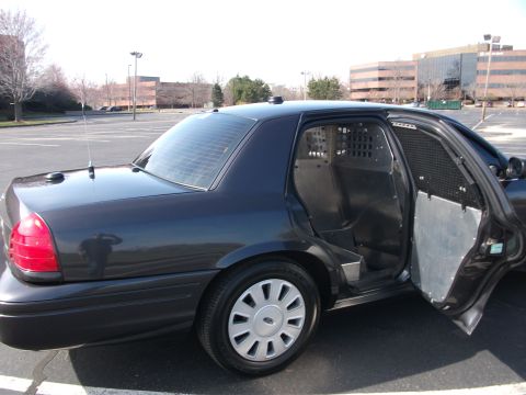 2001 Ford Crown Victoria - A dark sedan, likely a 2001 Ford Crown Victoria, is shown from the rear passenger side with its doors open.