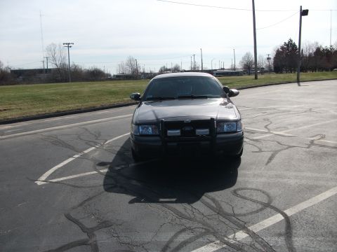 2001 Ford Crown Victoria - A dark 2001 Ford Crown Victoria, equipped with a push bar, is parked facing forward in a lot.