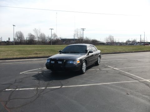 2001 Ford Crown Victoria - A Ford Crown Victoria police car is parked in an empty lot under a bright sky.