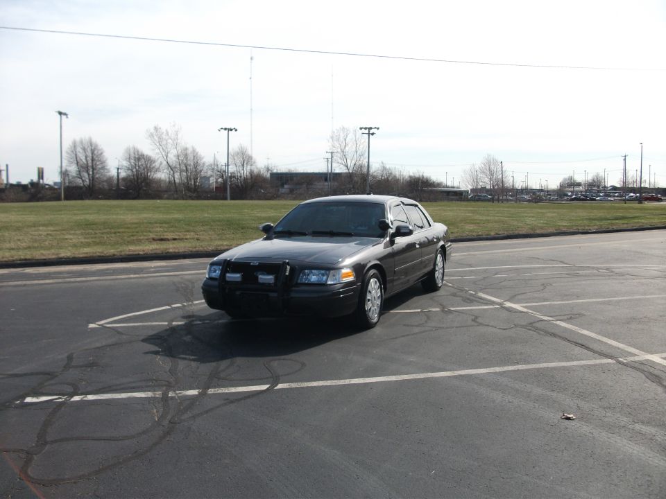 Dark gray Ford Crown Victoria police car parked in a lot. It has a push bumper on the front