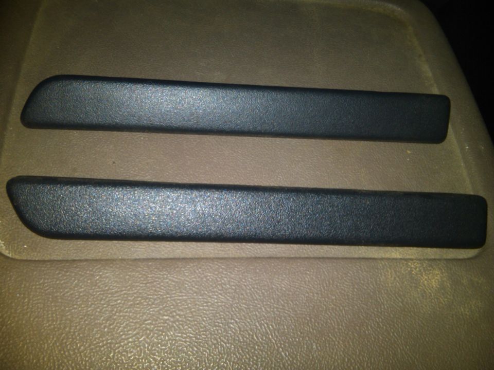 two black plastic trim pieces on a tan textured surface