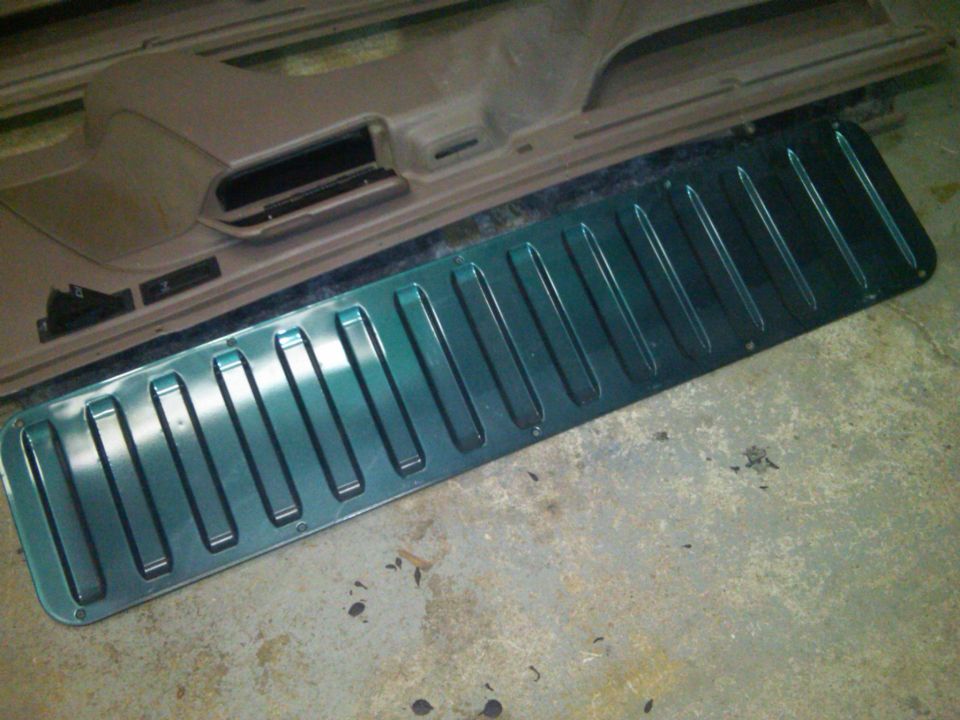 Green metallic trim piece with raised ribs lies on a beige car door panel