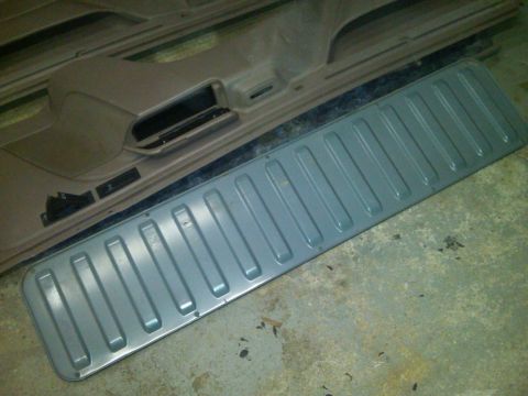1993 Ford Bronco - A tan interior door panel is shown next to a gray ribbed metal trim piece, likely for a vehicle.