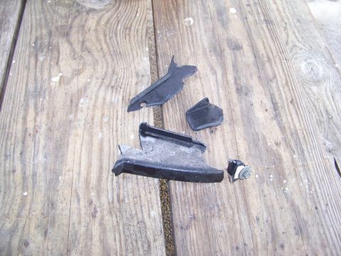 1987 Ford Ranger - Several pieces of broken black plastic automotive parts are scattered on a weathered wooden surface.