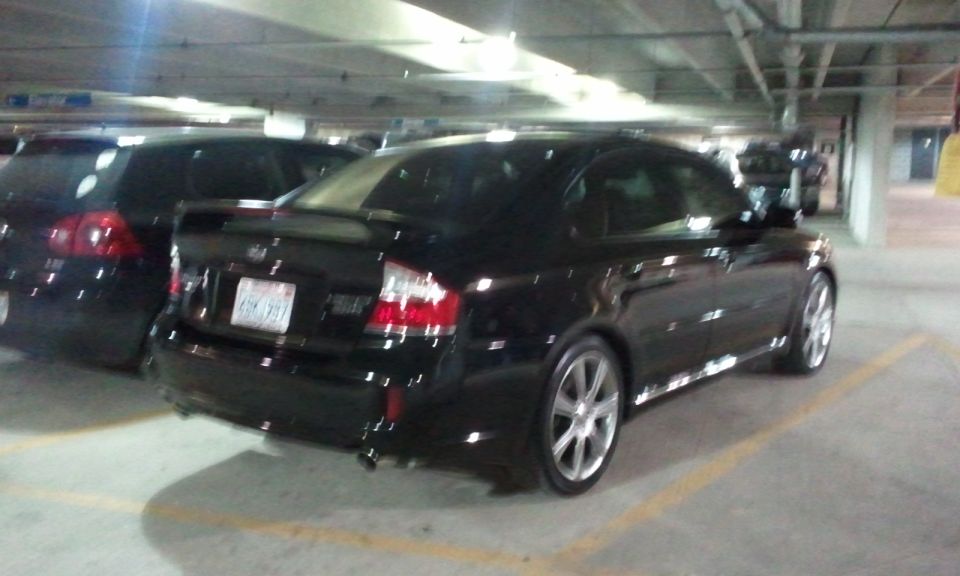 Black Subaru Legacy sedan parked in a garage, rear view. Another black car is parked to its left