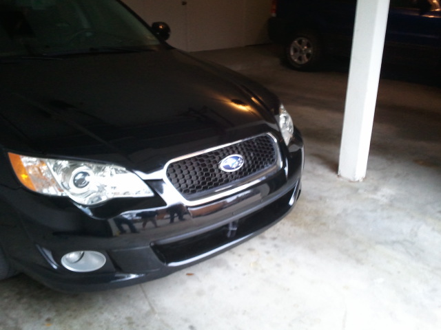 Front of a black Subaru sedan parked in a garage. Another dark vehicle is visible in the background