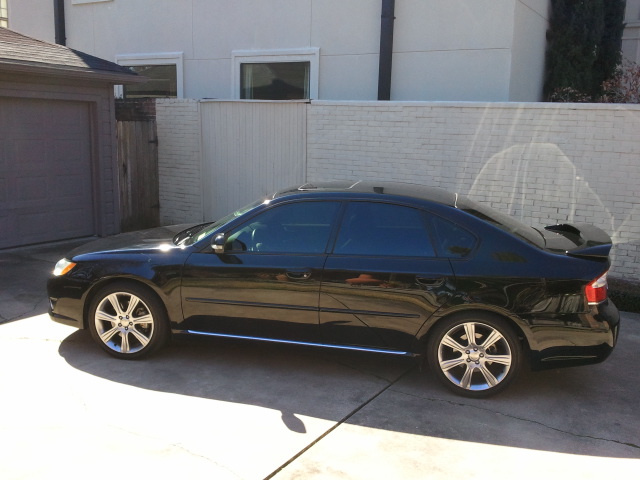 Black sedan parked in a driveway, side view. Sun glare on the paint