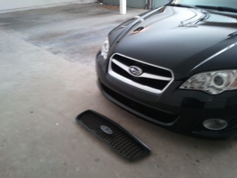 2008 Subaru Legacy - A black Subaru Legacy's front grille is detached and lying on the concrete floor next to the car.