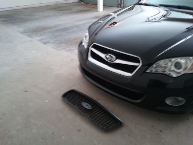 Black Subaru Legacy with its front grille removed and placed on the ground