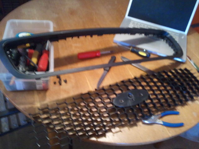 Car grill disassembled on a table with tools and a laptop nearby
