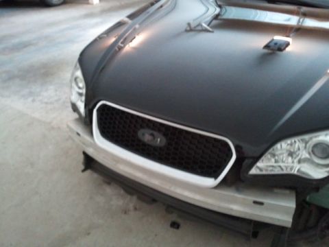 2008 Subaru Legacy - Close-up view of a car's front grille and headlights, a black hood and a white-trimmed grille.