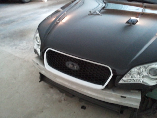 Front grille and headlights of a car with a black hood and white trim around the grille