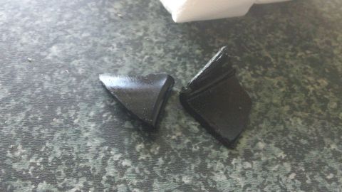 1994 Ford Bronco - Two fragments of black plastic, possibly from a vehicle part, are shown on a speckled countertop.