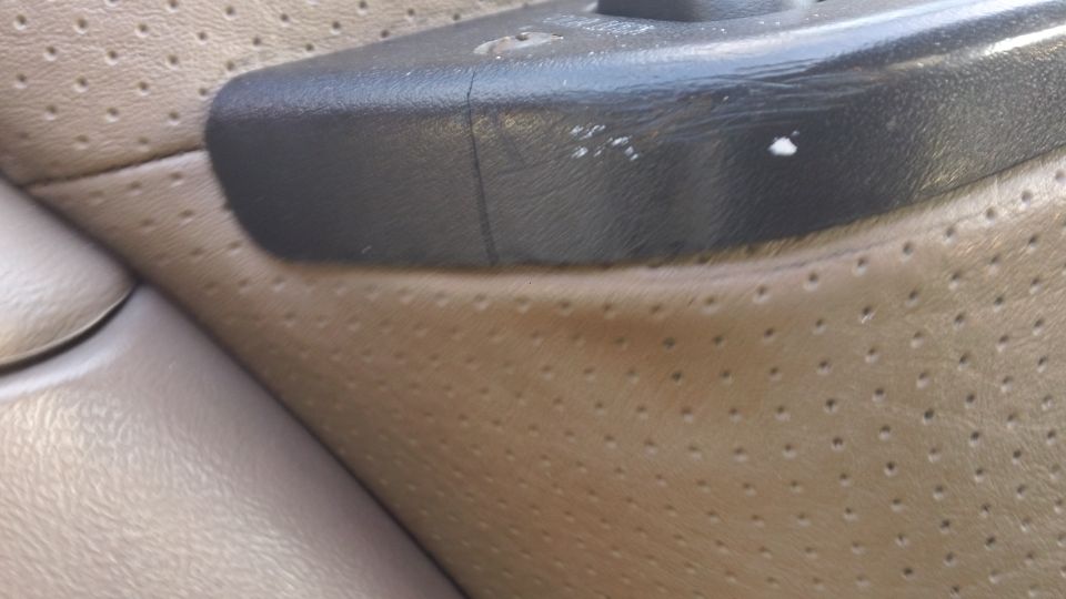 Tan perforated leather interior door panel with black plastic armrest showing white scuffs