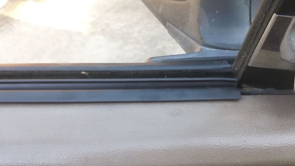 Close-up of a black rubber door seal against a tan interior panel, with a metal door frame visible